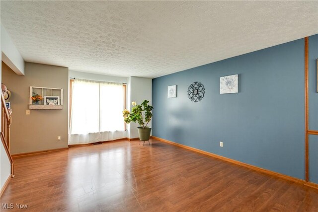 spare room featuring a textured ceiling, wood finished floors, and baseboards