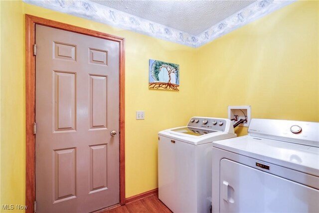 washroom featuring washing machine and dryer, a textured ceiling, light wood-style floors, and baseboards