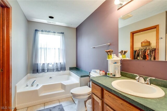 full bath featuring tile patterned floors, a garden tub, toilet, vanity, and a spacious closet
