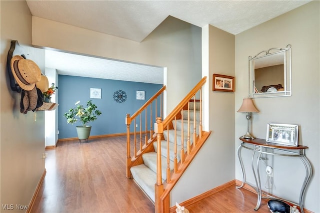 stairway featuring wood finished floors, baseboards, and a textured ceiling