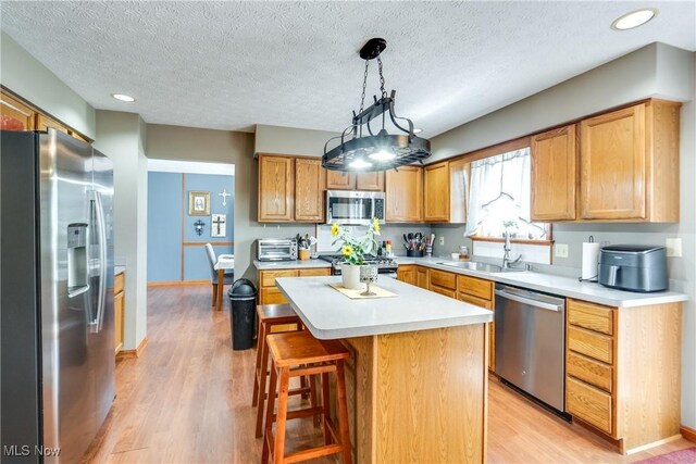 kitchen featuring appliances with stainless steel finishes, a sink, light wood-type flooring, light countertops, and a textured ceiling