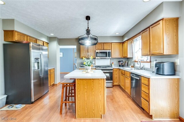 kitchen featuring stainless steel appliances, a sink, light countertops, light wood finished floors, and a textured ceiling