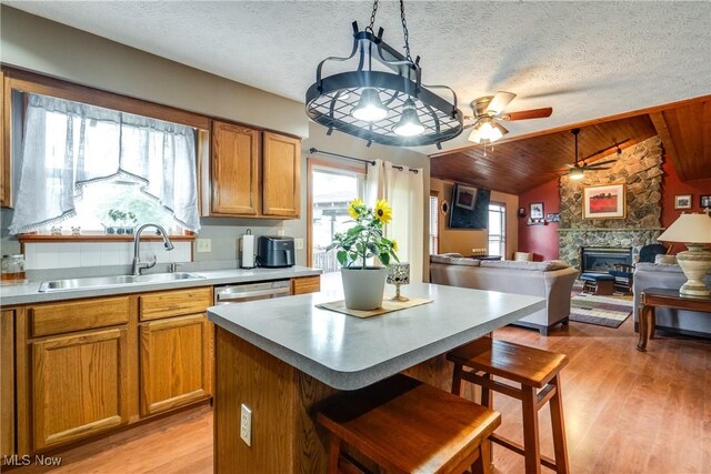 kitchen with a sink, a ceiling fan, a fireplace, light wood-style floors, and vaulted ceiling