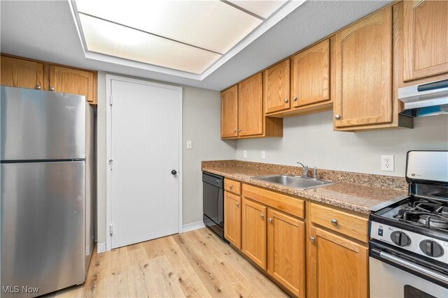 kitchen featuring appliances with stainless steel finishes, a sink, light wood-style floors, under cabinet range hood, and baseboards