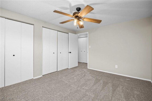 unfurnished bedroom featuring carpet floors, multiple closets, baseboards, and a ceiling fan