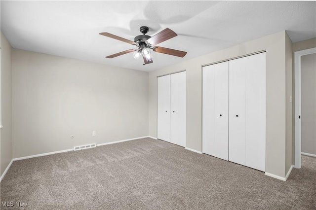unfurnished bedroom featuring carpet floors, multiple closets, baseboards, and ceiling fan