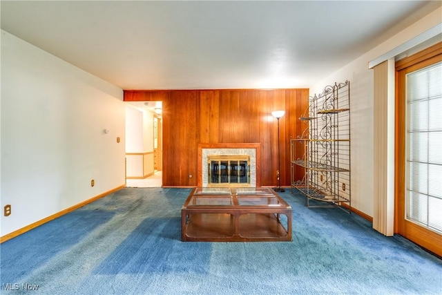 carpeted living room with a glass covered fireplace, baseboards, wooden walls, and healthy amount of natural light