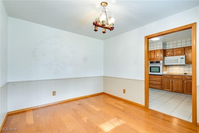 unfurnished dining area with light wood finished floors, a chandelier, and a wainscoted wall