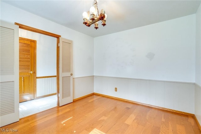 unfurnished room with a chandelier, wood finished floors, and baseboards