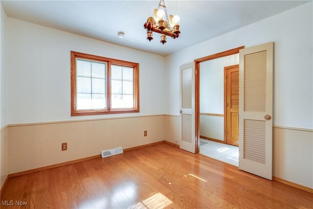 spare room with wood finished floors, a chandelier, a wainscoted wall, and baseboards