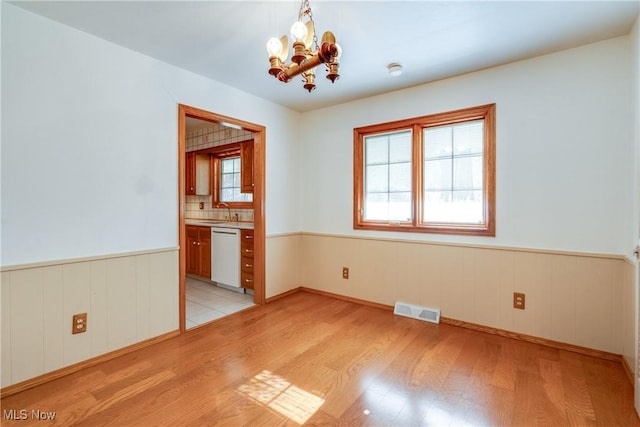 spare room with a chandelier, light wood-style floors, wainscoting, and a sink