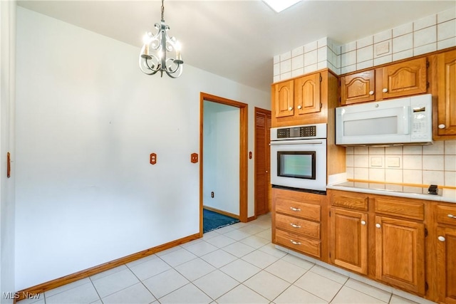 kitchen with white appliances, a chandelier, light countertops, brown cabinetry, and backsplash