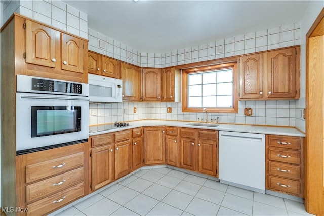 kitchen with white appliances, a sink, light countertops, and brown cabinetry