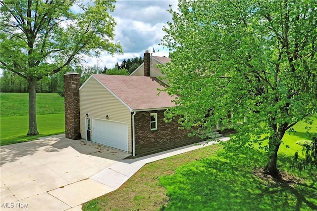 view of side of home featuring brick siding, a chimney, concrete driveway, a yard, and an attached garage