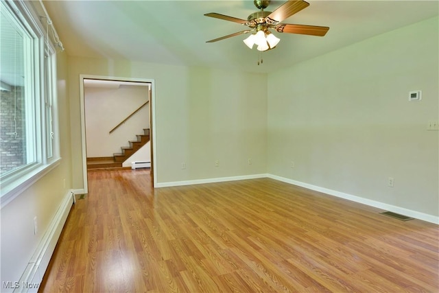 unfurnished room with baseboard heating, stairway, light wood-type flooring, and ceiling fan