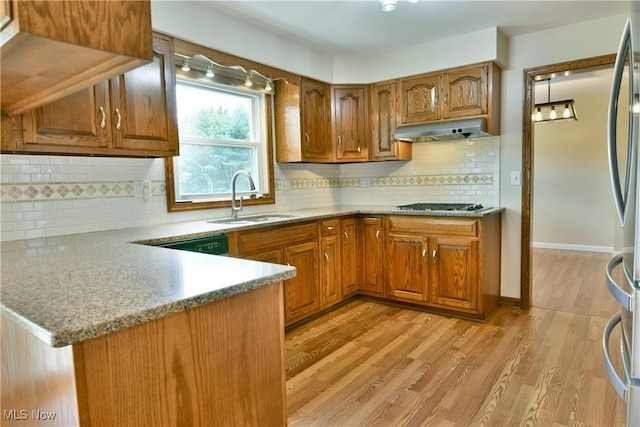 kitchen with a sink, under cabinet range hood, brown cabinetry, and backsplash