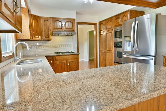 kitchen with appliances with stainless steel finishes, a sink, under cabinet range hood, and brown cabinetry
