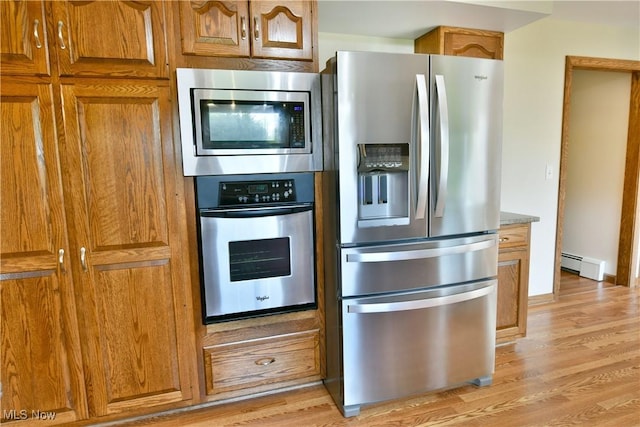 kitchen with appliances with stainless steel finishes, baseboard heating, light wood-type flooring, and brown cabinets
