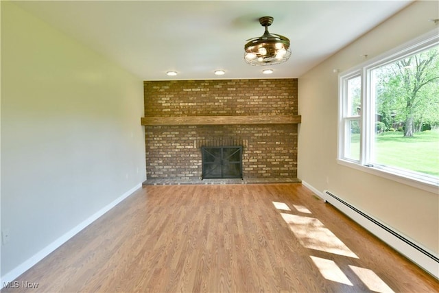 unfurnished living room featuring a baseboard heating unit, baseboards, wood finished floors, and a brick fireplace