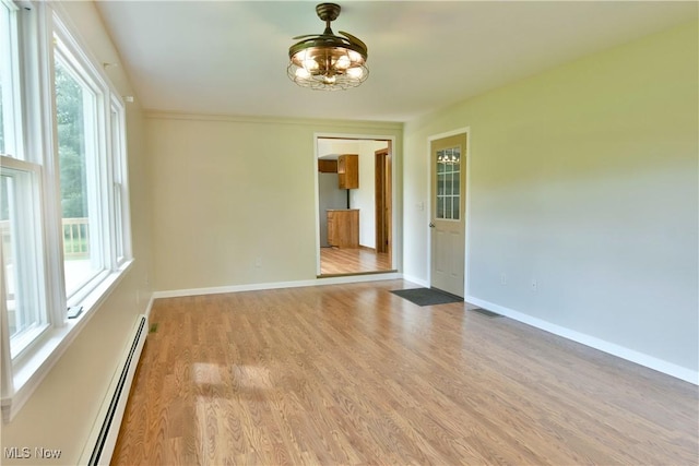 spare room featuring baseboard heating, light wood-type flooring, a chandelier, and plenty of natural light