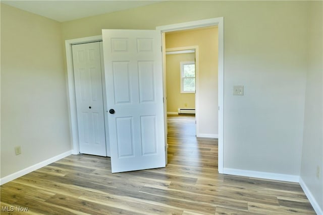 unfurnished bedroom with a baseboard heating unit, baseboards, and wood finished floors