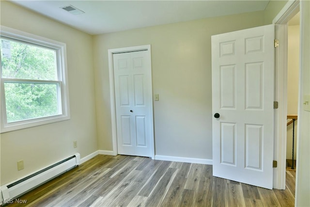 unfurnished bedroom featuring a baseboard heating unit, wood finished floors, a closet, and baseboards