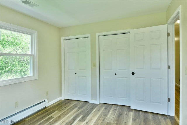 unfurnished bedroom featuring a baseboard heating unit, wood finished floors, and baseboards