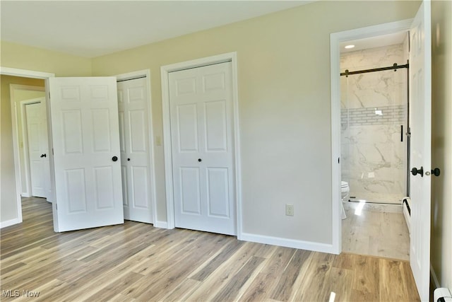 unfurnished bedroom featuring two closets, light wood finished floors, baseboards, connected bathroom, and a baseboard heating unit