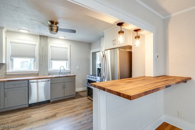 kitchen with stainless steel appliances, butcher block countertops, gray cabinets, light wood finished floors, and crown molding