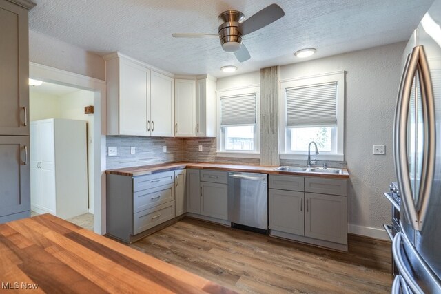 kitchen featuring a sink, stainless steel appliances, butcher block countertops, gray cabinetry, and wood finished floors