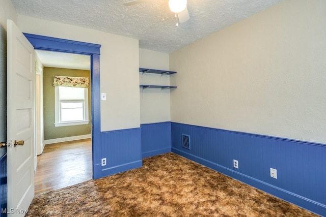 unfurnished room with a wainscoted wall, a textured ceiling, a ceiling fan, and carpet floors