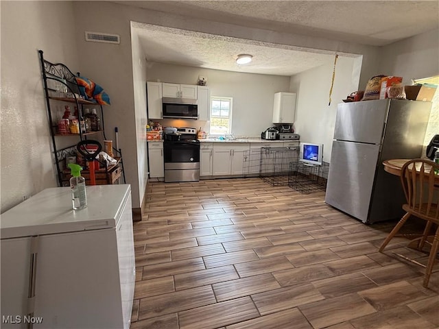 939 S Arch Ave, Alliance, OH 44601 - kitchen featuring stainless steel appliances, wood tiled floors, white cabinetry, light countertops, and a textured ceiling