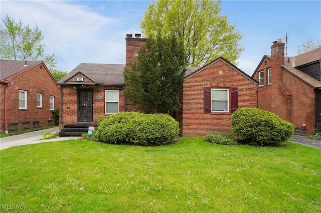 view of front of house with brick siding, a front lawn, a chimney, and roof with shingles