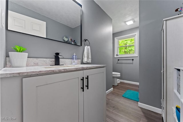 bathroom featuring vanity, baseboards, toilet, wood finished floors, and a textured ceiling
