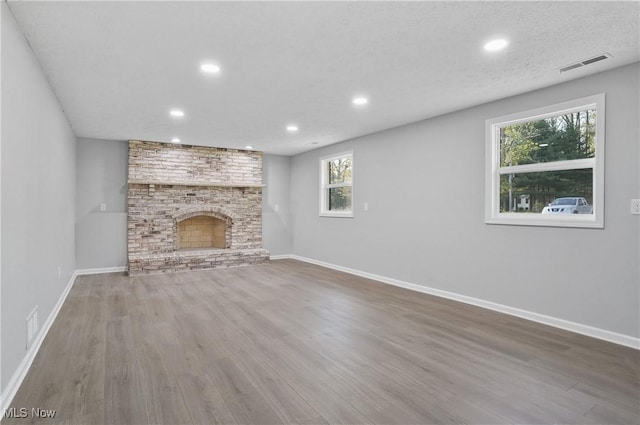 unfurnished living room featuring wood finished floors, recessed lighting, baseboards, and a brick fireplace