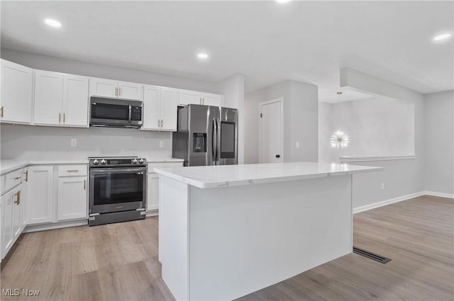 kitchen with appliances with stainless steel finishes, light wood-style flooring, a center island, white cabinets, and recessed lighting
