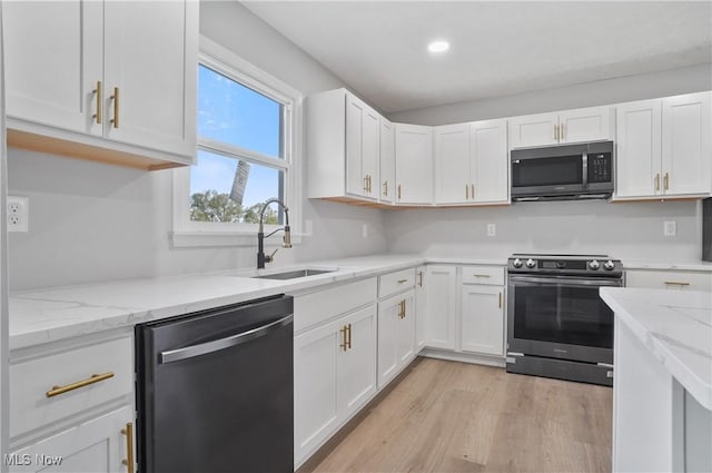 kitchen featuring appliances with stainless steel finishes, a sink, white cabinetry, light stone countertops, and light wood-style floors