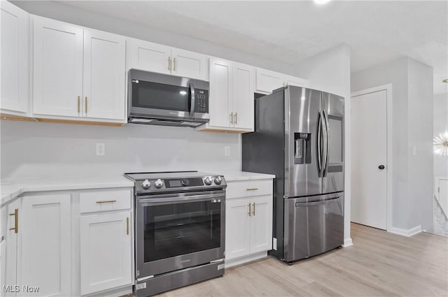 kitchen with stainless steel appliances, white cabinets, light wood-style floors, and baseboards
