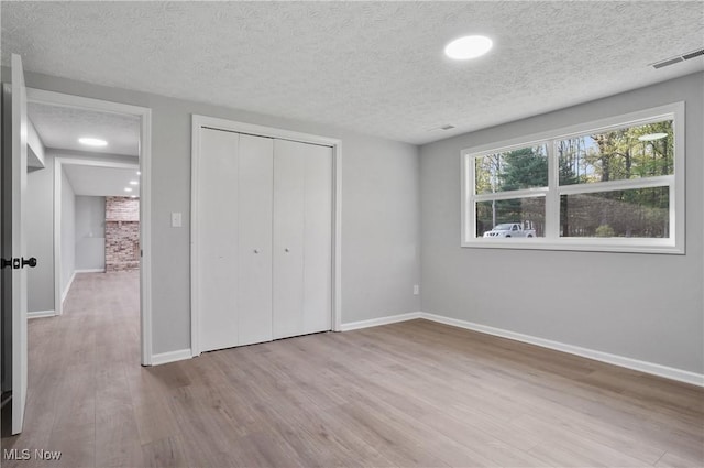 unfurnished bedroom with wood finished floors, baseboards, a textured ceiling, and a closet