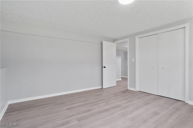 unfurnished bedroom featuring wood finished floors, a textured ceiling, baseboards, and a closet