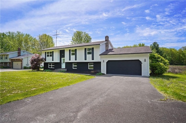 bi-level home featuring a front yard, a chimney, a garage, and driveway