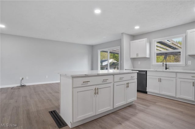 kitchen with stainless steel dishwasher, light wood finished floors, light countertops, a center island, and white cabinets
