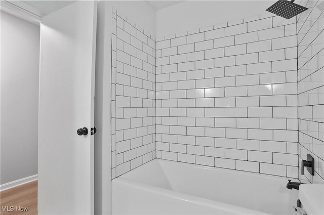 bathroom with washtub / shower combination, wood finished floors, and baseboards