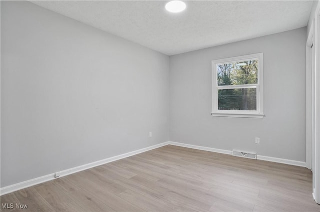 spare room with light wood finished floors, baseboards, and a textured ceiling