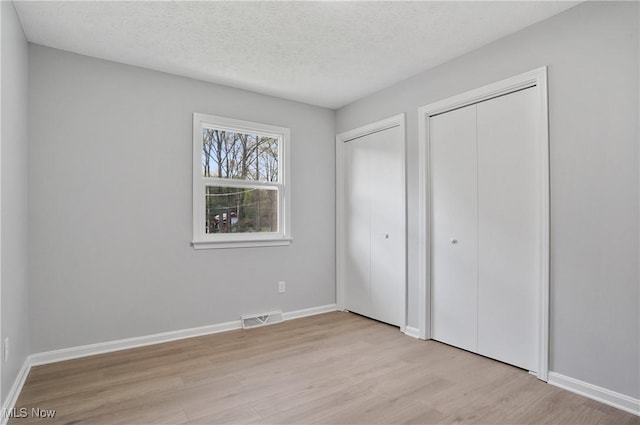 unfurnished bedroom featuring light wood-style floors, two closets, baseboards, and a textured ceiling