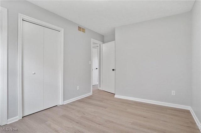 unfurnished bedroom featuring light wood-type flooring, baseboards, and a closet