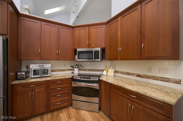 kitchen featuring appliances with stainless steel finishes, lofted ceiling, decorative backsplash, light wood-style flooring, and a skylight