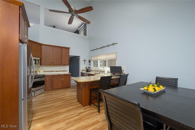 kitchen featuring appliances with stainless steel finishes, a peninsula, high vaulted ceiling, a sink, and light wood-style floors