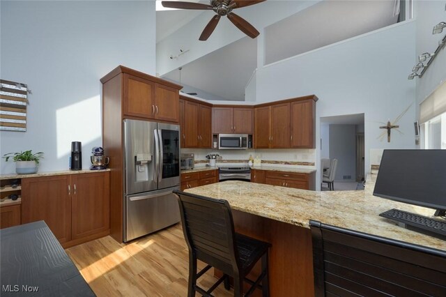 kitchen with stainless steel appliances, high vaulted ceiling, a ceiling fan, light wood-style floors, and light stone countertops