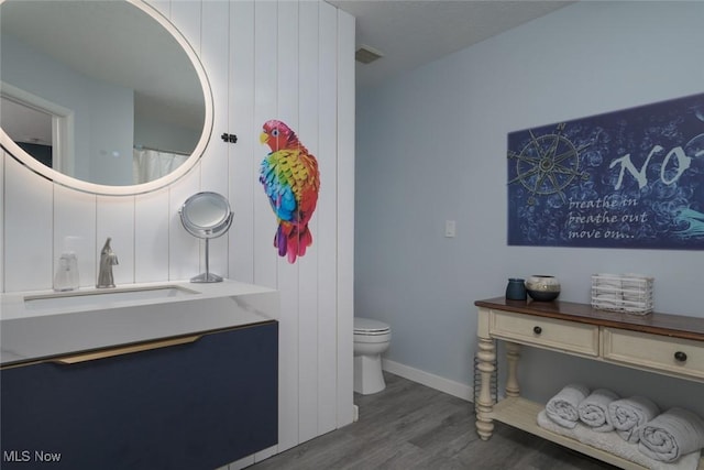 full bath featuring wood finished floors, toilet, vanity, and baseboards